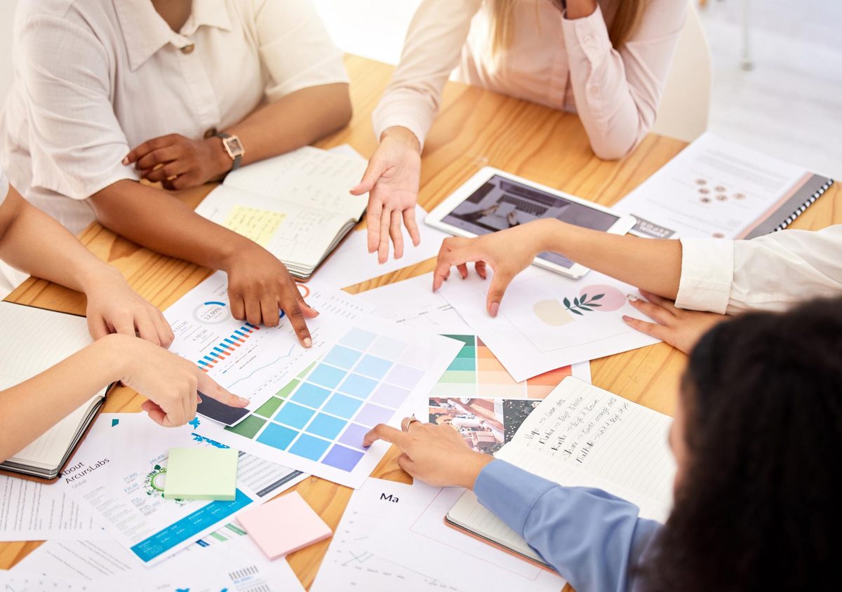 Team members pointing at colour swatches, charts and handwritten brand notes spread across a table