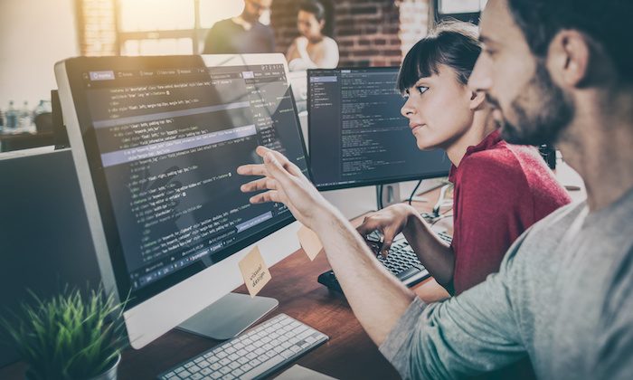 Two colleagues reviewing website code on desktop monitors
