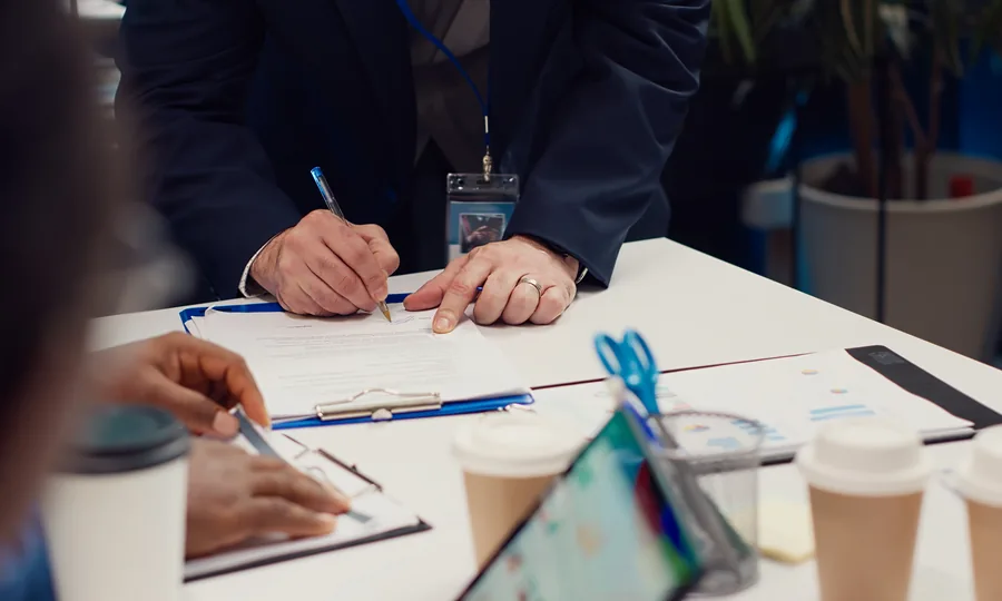 A person signing a document on a clipboard during a meeting